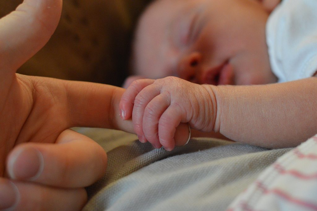 Uyuyan bir bebek, minik eliyle bir büyüğünün parmağını tutuyor.